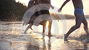 Group of happy friends at sunset running into water getting wet and making splashes swimming in the sea