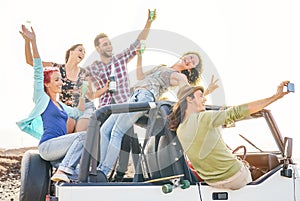 Group of happy friends taking selfie with mobile smart phone on convertible car - Young people having fun making party