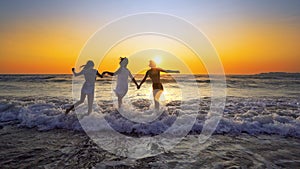 Group of happy girls jump into the ocean at sunset