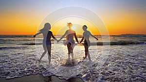Group of happy girls jump over sea waves at the beach at sunset