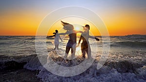 Group of happy girls jump over sea waves at the beach on sunset