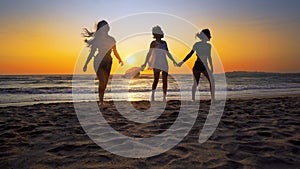 Group of happy girls running and playing on sand at sunset