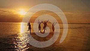 Group of happy girls running and playing in water at the beach on sunset dancing, spraying over summer sunset. Beach