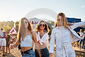 Group of happy girls at summer beach music fest, dancing, laughing in sun. Friends enjoy live concert, fun outdoor event