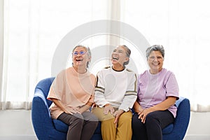 The group of happy and healthy three Asian senior women sits together on a sofa. Smiling and laughing together.