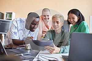 Group of happy intercultural students discussing data on screen of tablet