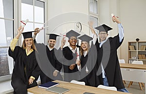 Group of happy joyful diverse university graduates in caps and gowns holding up diplomas