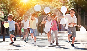 Group of happy kids with balloons running in race in the street