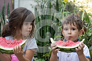 Group of happy kids eating watermelon on grass in summer park. Children with watermelon.