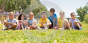 Group of happy kids friends resting on grass together in park