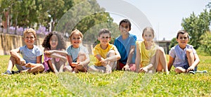 Group of happy kids friends resting on grass together in park