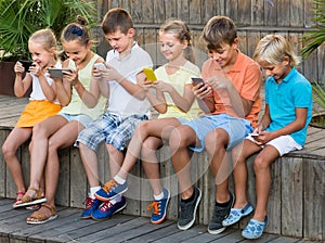 Group of happy kids playing with mobile phones outdoors