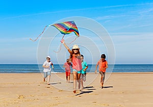 Group of happy kids run with kite on the beach