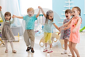 Group of happy kindergarten kids jumping raising hands while having fun in entertainment center