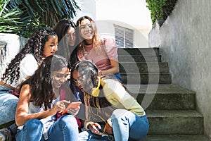 Group of happy Latina teen girls in a bleacher using their cell phones or smartphones to view photos or chat