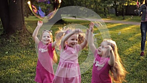 Group of happy little children girl playing trying catch big air soap bubble blower