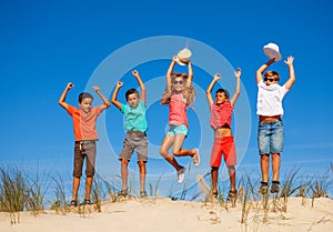 Group of happy little kids jump on sand dune up