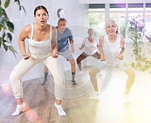 Group of happy mature sports women and man in activewear exercising dynamic dancing movemens in gym studio