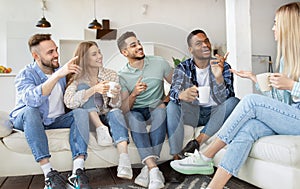 Group of happy millennial friends drinking tea, having talk, enjoying time together at home