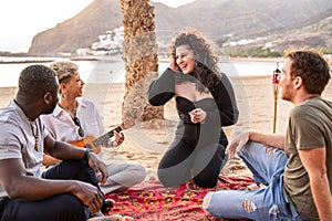 Group of happy multicultural friends having fun together on the beach, laughing, playing music and singing together