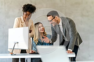 Group of happy multiethnic business people in formal wear gathered around computer in office