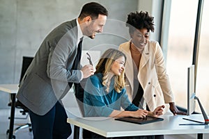 Group of happy multiethnic business people in formal wear gathered around computer in office