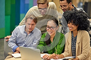 Group of happy multiracial business people sitting at desk in the modern coworking space, looking at laptop screen and