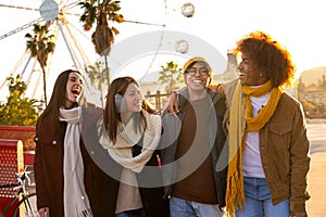 Group of happy multiracial college student friends laughing embracing together while walking around city on a winter day