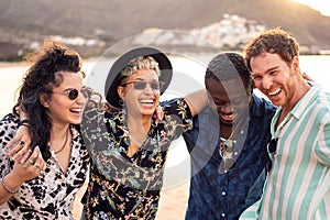 Group of happy multiracial friends having fun together on the beach, dancing and laughing. Mixed race people friendship concept.