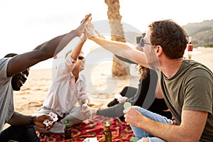 Group of happy multiracial friends having fun together on the beach, playing cards on picnic, laughing. Mixed race people
