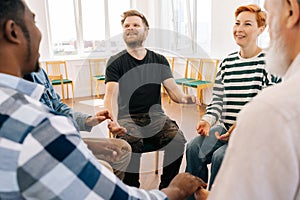 Group of happy multiracial people holding hands sitting in circle during therapy session. Cheerful multicultural and