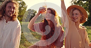 Group of happy people cheering with glass bottles while having picnic. Diverse young friends laughing and spending time