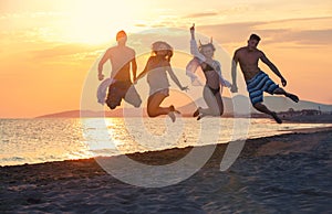 Group of happy people dancing and jumping inside sea on sunset