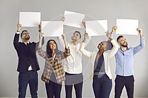 Group of happy people standing on gray background and holding white mockup banners