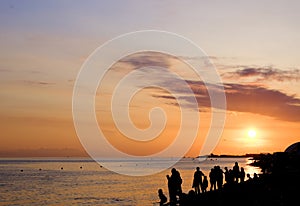 Group of happy people and their silhouettes that are on the beach against the sunset. Beautiful landscape of the ocean or the sea