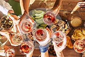 Group of happy people toasting  together with cups of red wine under the sun light in a sunny day - outdoor leisure activity for