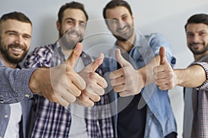 Group of happy positive young men standing together and showing thumbs up gesture