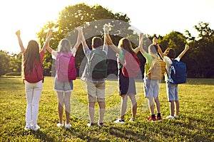 Group of happy school children standing in park, holding hands and looking at sunset