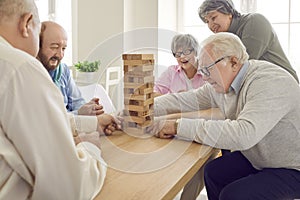 Group of happy senior people playing with wooden tower board game in retirement home