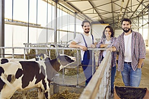 Group of happy farm workers standing near cage with calves in barn on livestock farm