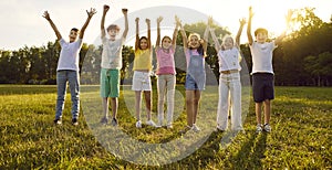 Group of happy smiling kids friends having fun and raising hands up in the park standing in a line.