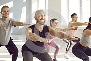 Group of happy, smiling young people doing squats during a fitness workout at the gym