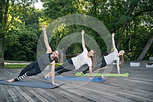 Group of happy smiling young women practice yoga early in the morning outdoors. Side Plank. Vasishthasana