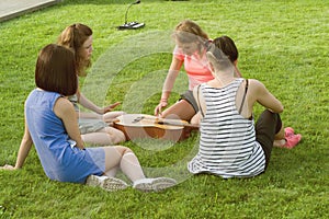 Group of happy teenage girls having fun outdoors with guitar. Come up with new music, sit on green lawn in the yard.