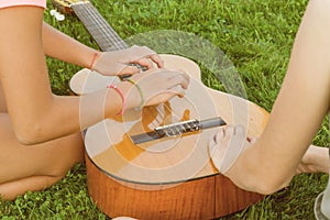 Group of happy teenage girls having fun outdoors with guitar. Come up with new music, sit on green lawn in the yard.