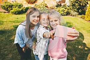 Group of happy teenage girls laughing and taking a selfie on a mobile phone outdoors.