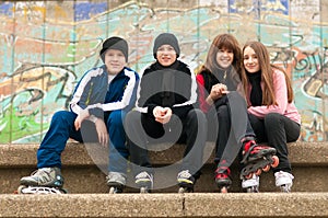 Group of happy teenagers sitting on the street in roller skates