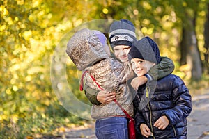 Group of happy three kids having fun outdoors in autumn park. Cute children enjoy hugging together against golden fall background.