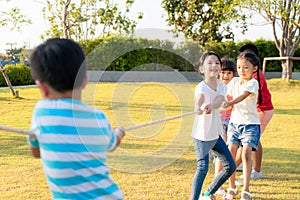 Group of happy young Asian children playing tug of war or pull rope togerther outside in city park playground in summer day.