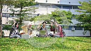 A group of happy young Asian-diverse college students are sitting on the grass in the park together